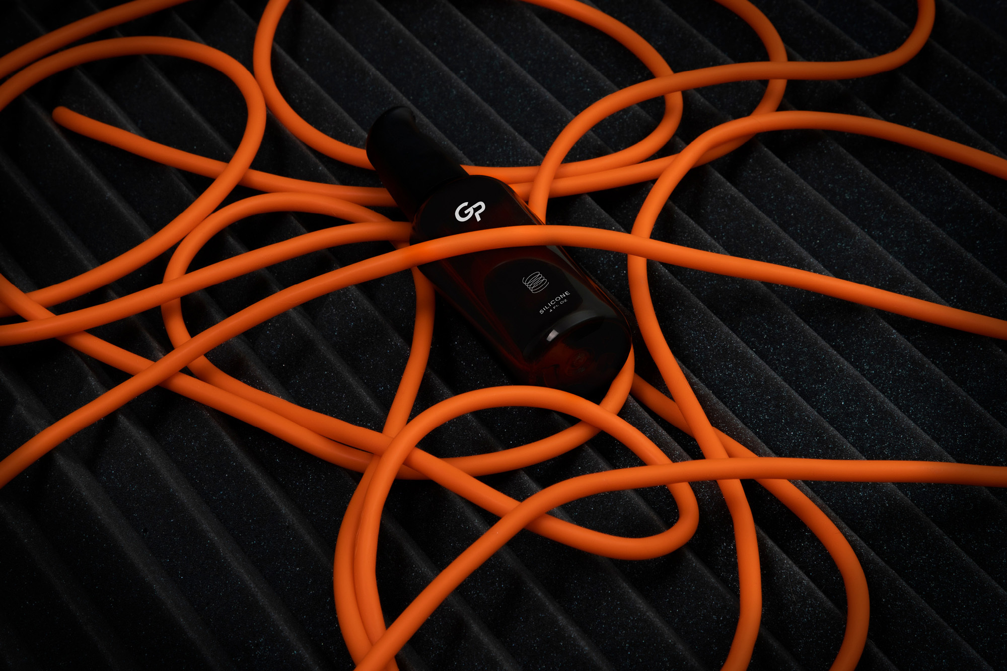 Product shot of a dark brown bottle with orange cord on a dark grey background, showcasing modern aesthetic and design elements.