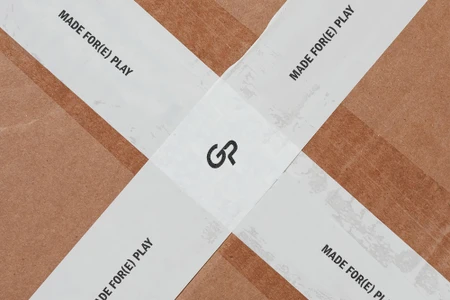Cardboard box sealed with white packing tape displaying printed text and a centered monogram logo