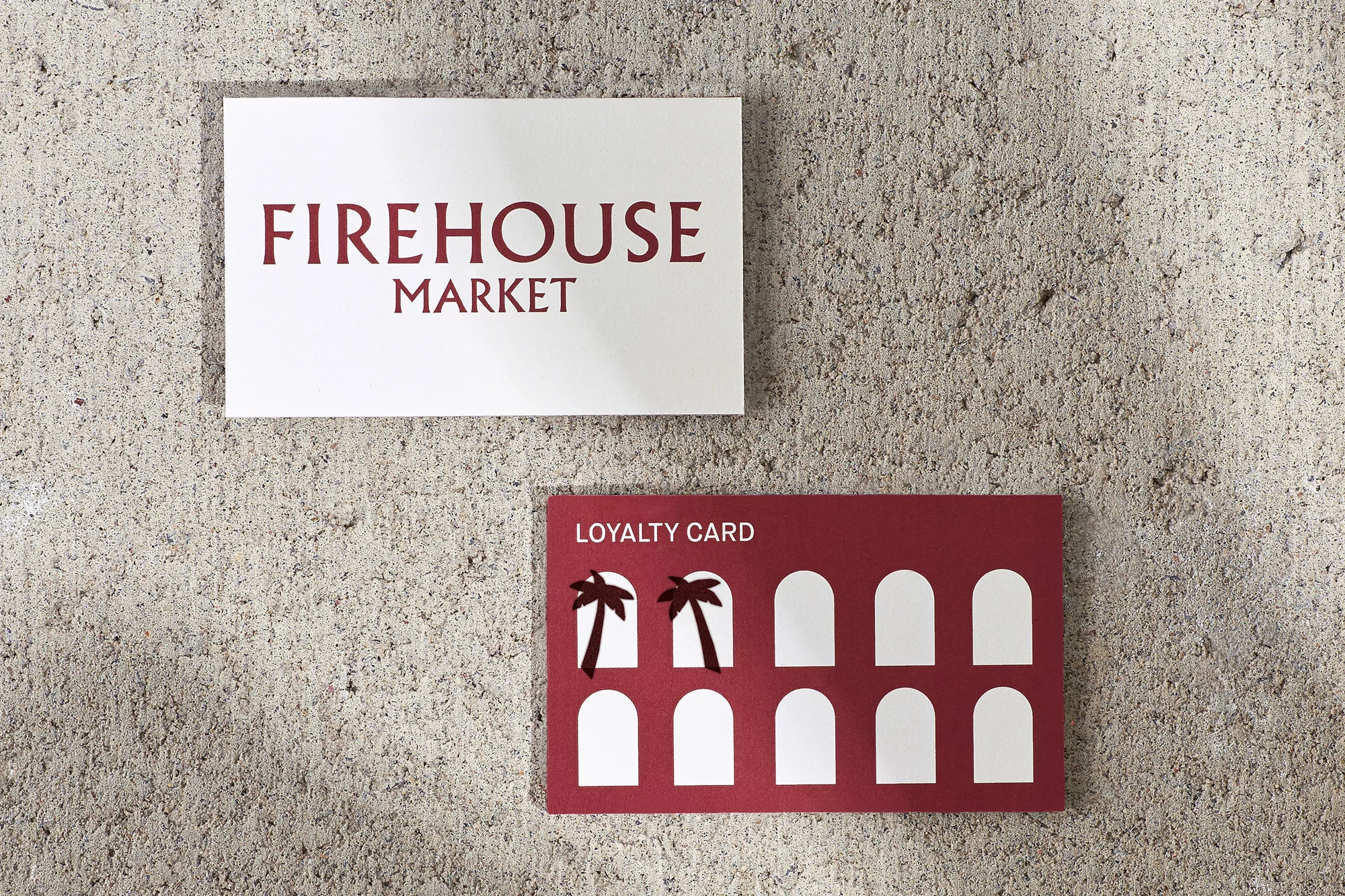 Promotional material on a gray concrete surface. Signage for Firehouse Market with a maroon loyalty card and palm tree design.