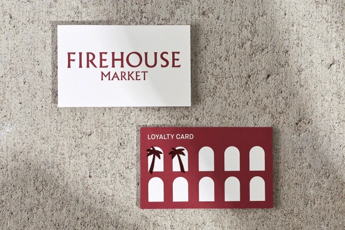 Promotional material on a gray concrete surface. Signage for Firehouse Market with a maroon loyalty card and palm tree design.