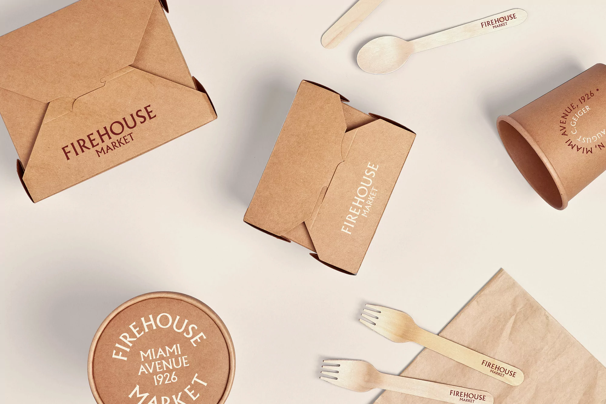 Overhead shot of disposable food containers and wooden cutlery branded with 'Firehouse Market' logo on a light cream background.