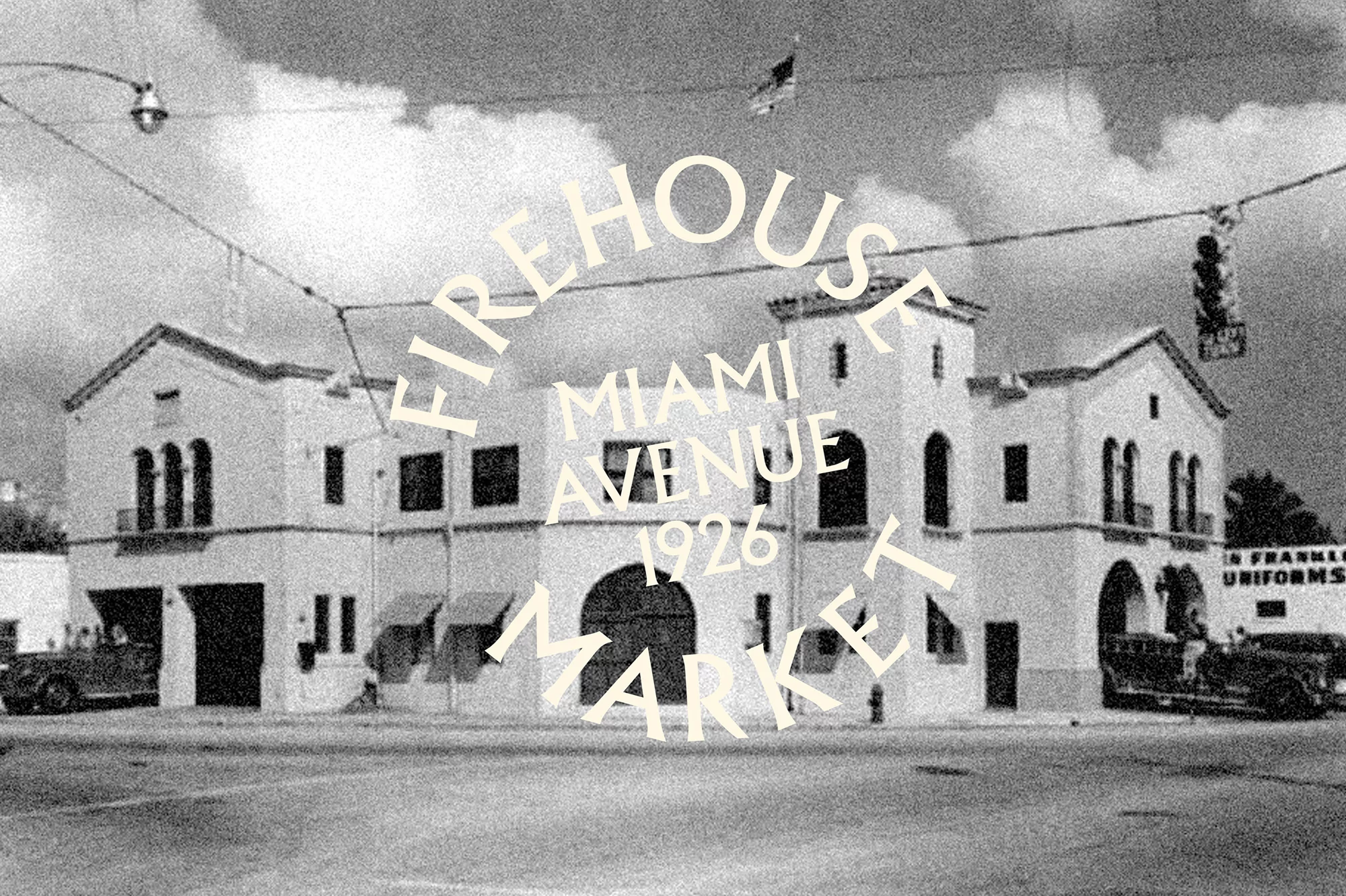 Monochrome photo of a historic Firehouse Market building in Miami, 1926, featuring vintage vehicles and a cloudy sky.