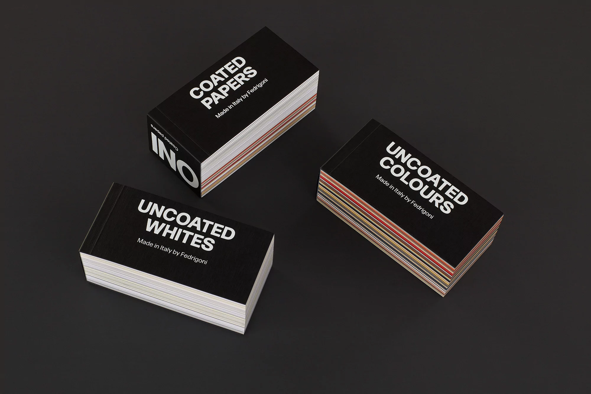 Close-up of three stacks of black paper sample books on a dark surface, featuring 'Coated Papers', 'Uncoated Whites' and 'Uncoated Colors'.