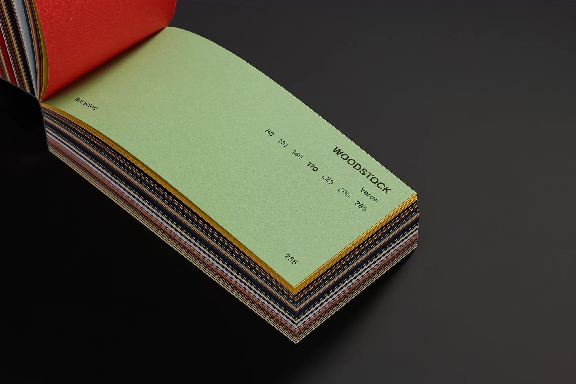 Open swatch book featuring green pages with black text on a dark gray surface, angled close-up view, emphasizing texture and color.