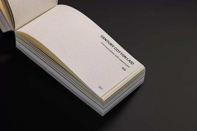 Close-up of a paper sample book with textured white pages, displayed against a dark gray surface, showcasing different paper stock options.