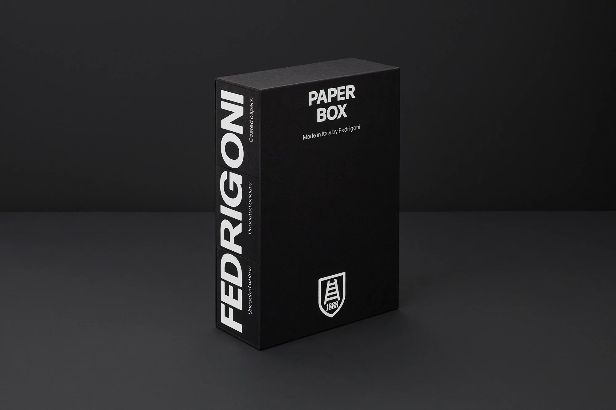 Black Fedrigoni paper box in a studio shot with a paper texture effect, set against a dark gray background, showcasing brand logo and text.