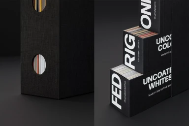 Black Fedrigoni paper swatch boxes with white typography stacked on a dark surface against a dark background