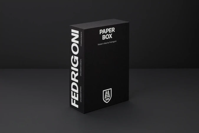 Black rectangular paper box with white typography standing upright on a dark grey surface
