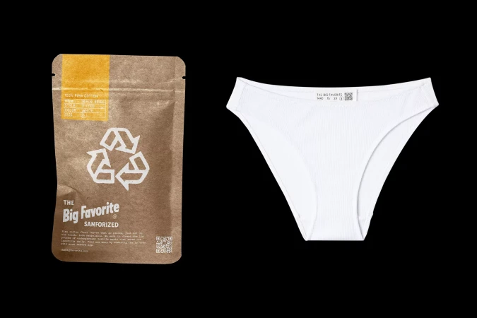 Image of a brown paper package with recycling symbol next to a pair of white ribbed briefs on a black backdrop.
