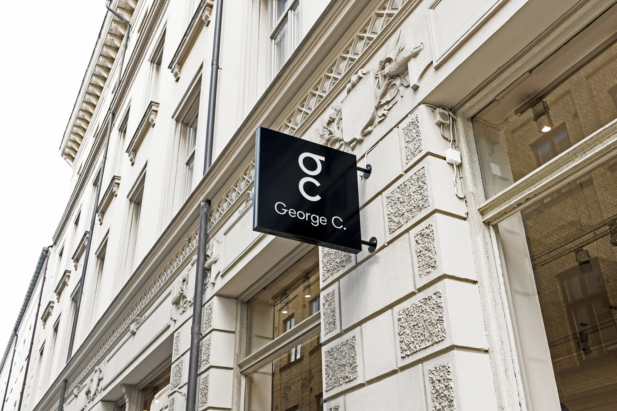 Exterior of a building with a George C. logo sign on a black background. Facade shows ornate architectural details on a sunny day.