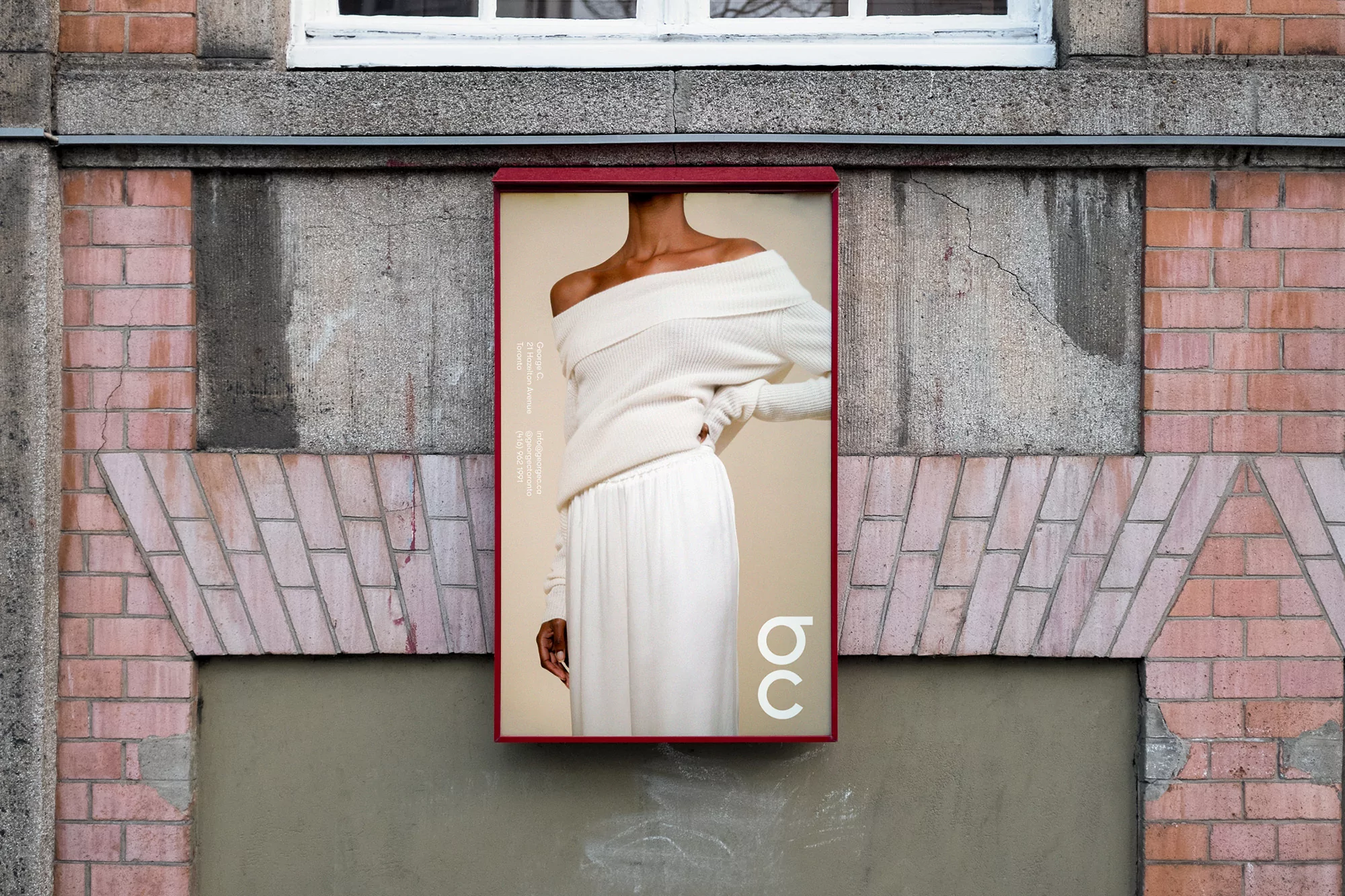 An illuminated outdoor billboard displaying a model wearing an off-the-shoulder cream sweater mounted on a weathered brick wall.