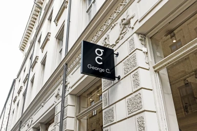 Black square storefront sign with white logo mounted on the stone exterior wall of a classic building