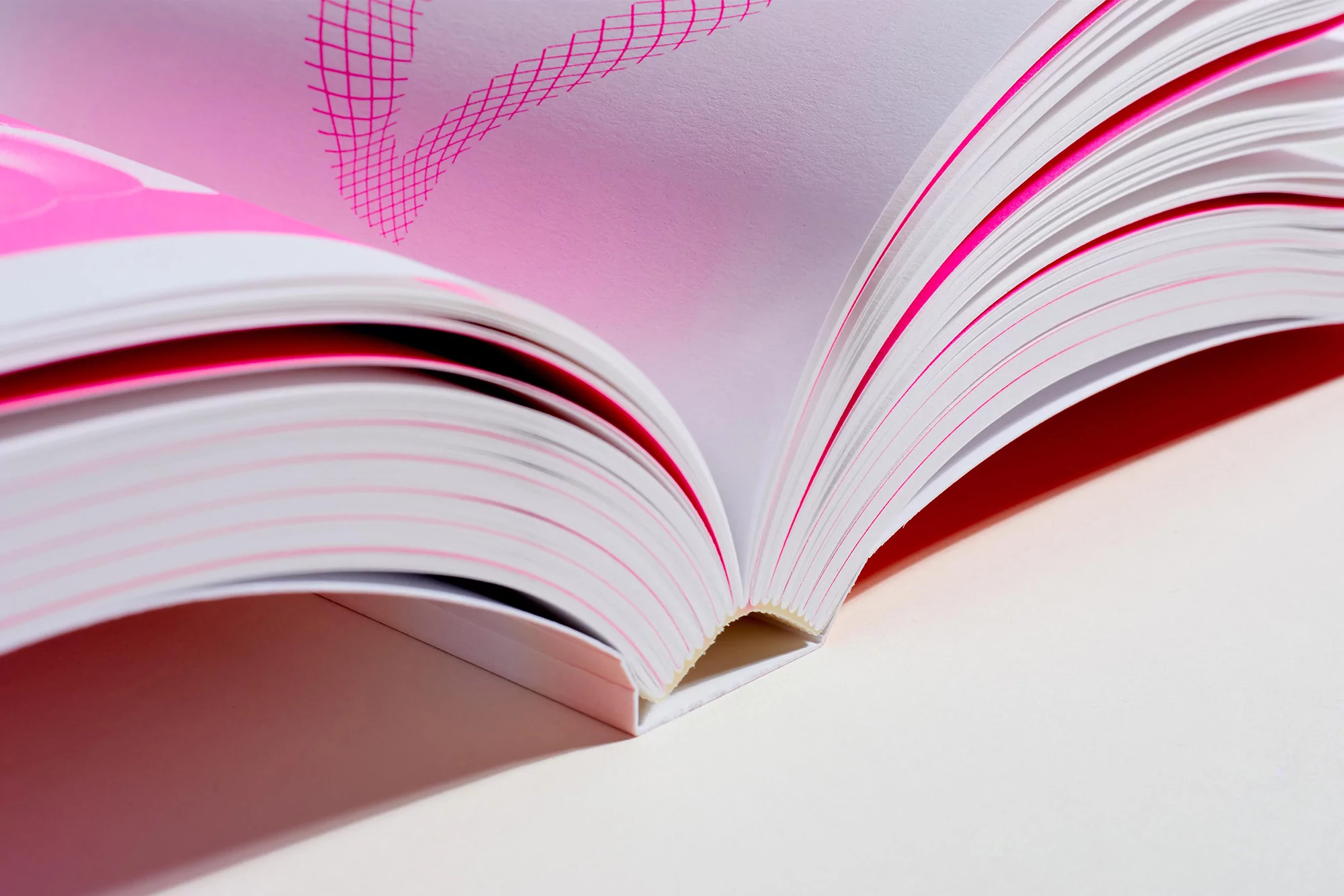 Open book with pink details. Pages of a book spread open, showing pink lined paper and white pages against a white background.
