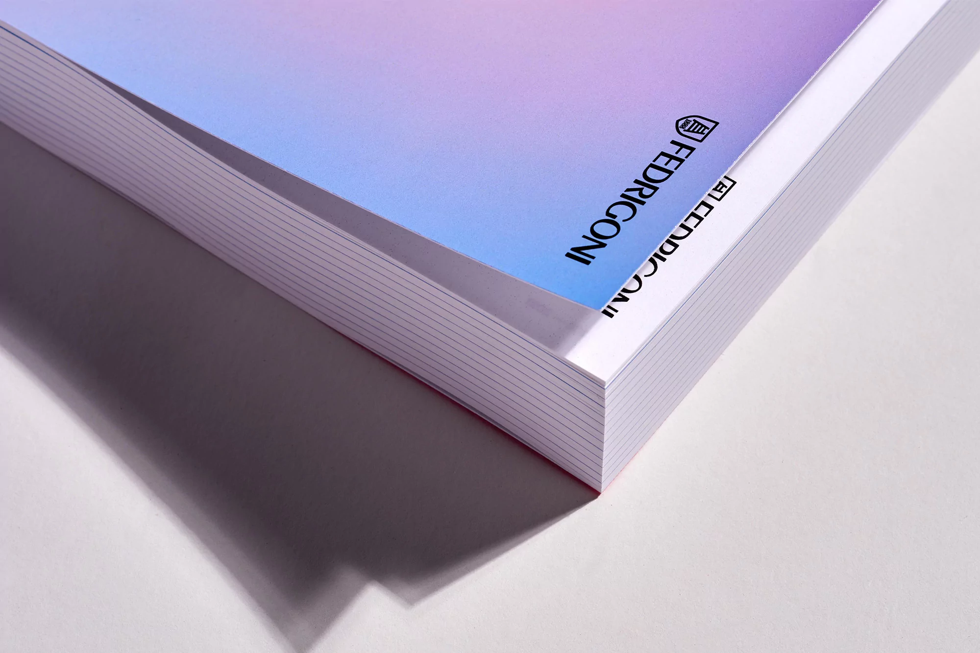 Close-up shot of a thick book with the FEDRIGONI logo in an indoor setting, showcasing white pages and a colored cover.