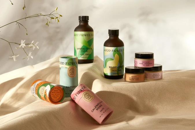 Botanical skincare products by Good Flower Farm displayed on a neutral surface with soft lighting and sprig of delicate flowers.