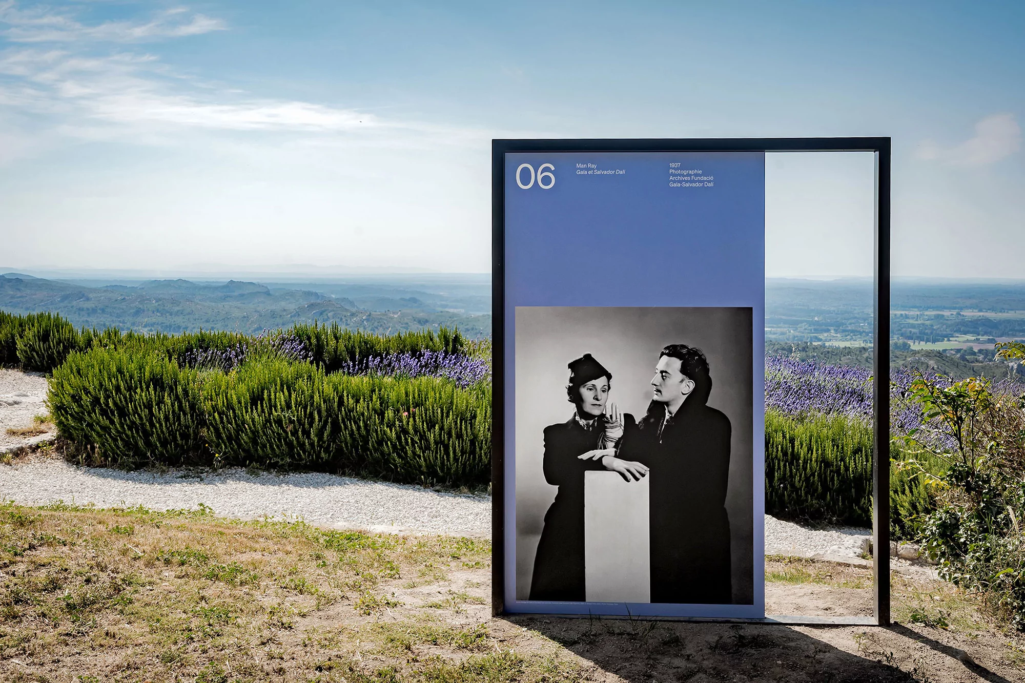Outdoor installation features a black-and-white portrait of two adults in front of a landscape with lavender bushes and a blue sky.