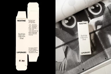 Unfolded and assembled white product packaging boxes for ROOTINE Austrian CBD against a black and printed magazine page background.
