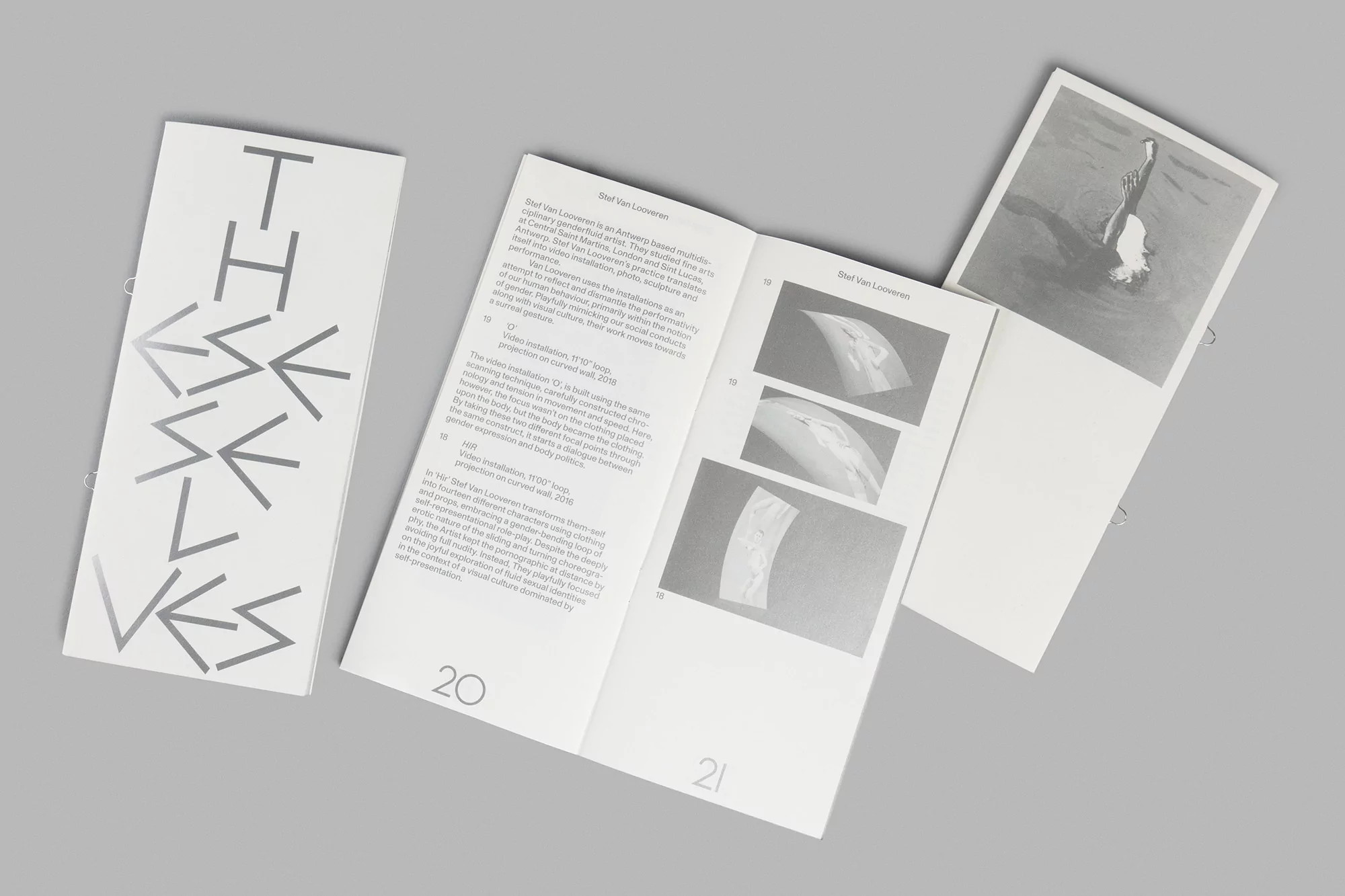 Three open books are displayed on a gray surface, featuring text and black-and-white images, offering a glimpse into its contents.