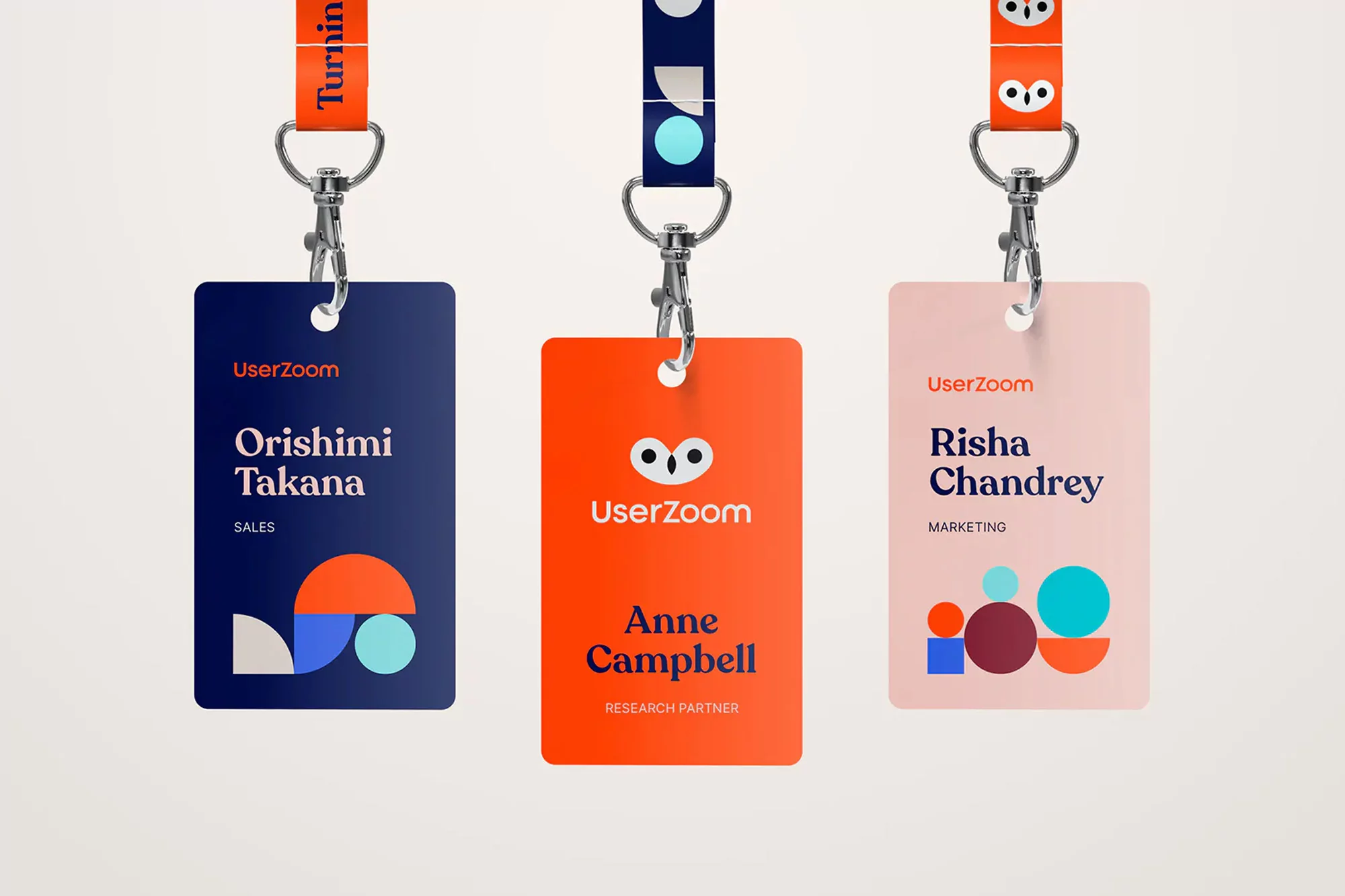 Three employee ID badges from UserZoom hang against a white background; each badge displays the company logo and employee information.