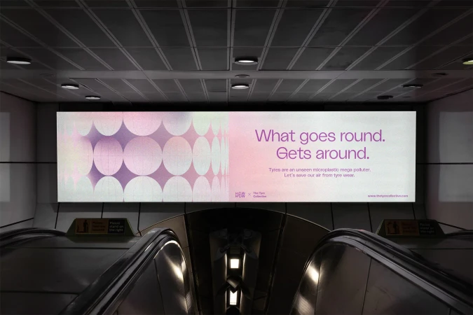 Eye-level, indoor shot of an advertisement in an underground station, featuring purple circles and text about tyre pollution.