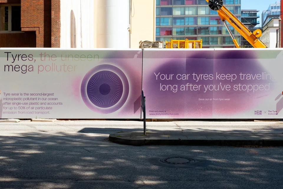 Eye-catching outdoor billboard promoting tyre recycling and environmental awareness on a city street, with a crane visible in background.