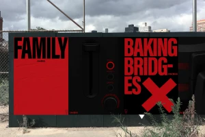 Outdoor poster installation with bold black and red typography reading family and baking bridges against a dark industrial backdrop.