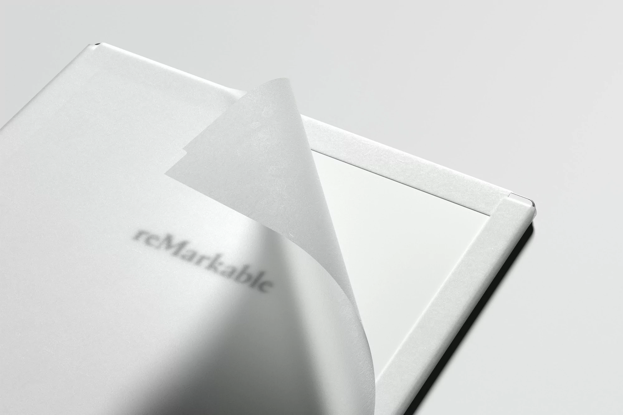 Close-up shot of a white reMarkable tablet with the protective film partially peeled off, revealing the screen underneath, indoors.