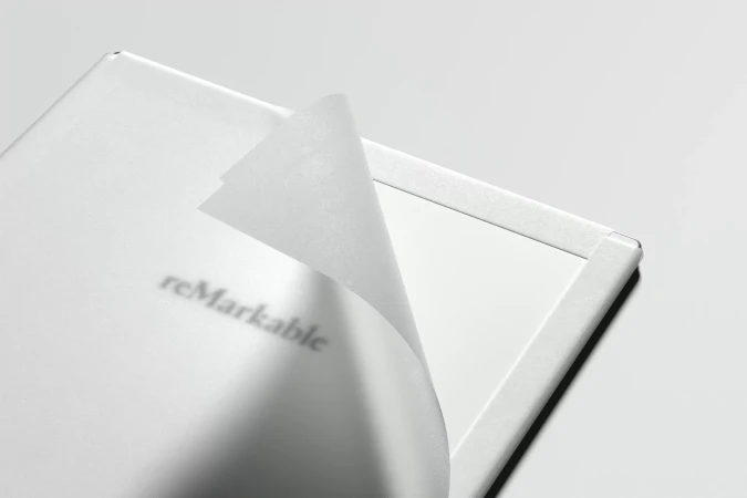 Close-up shot of a white reMarkable tablet with the protective film partially peeled off, revealing the screen underneath, indoors.