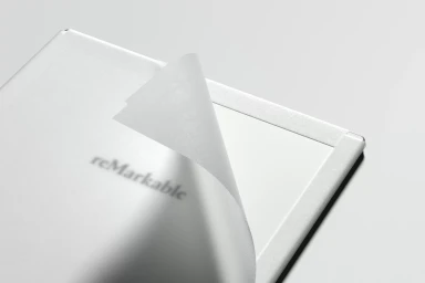 Close-up of a white reMarkable paper tablet with a translucent page lifting up, set against a clean grey background.