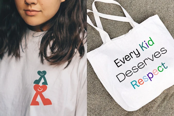 Brunette woman in white tee with graphic next to a white tote bag with an equality message on a sandy surface, outdoor.