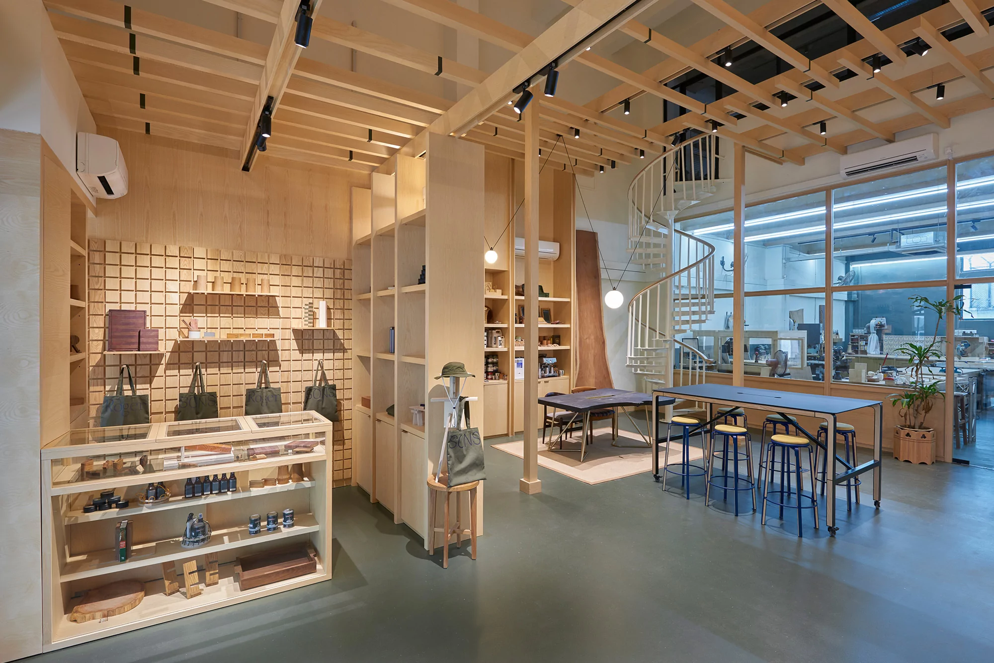 Retail store interior showcasing modern design with natural light, wooden fixtures, display shelves, tables, and a spiral staircase feature.