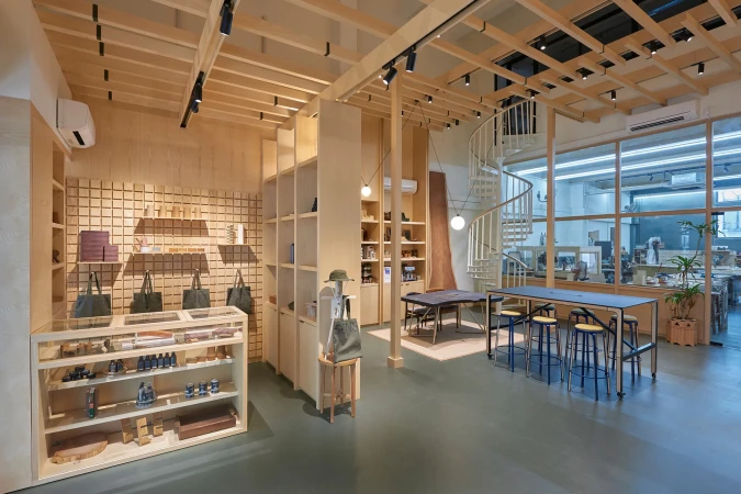 Retail store interior showcasing modern design with natural light, wooden fixtures, display shelves, tables, and a spiral staircase feature.