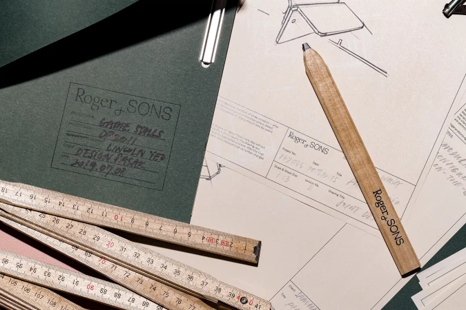 Close-up on architectural drawings, wooden folding ruler, and a pencil with a company logo, showcasing design and planning details.