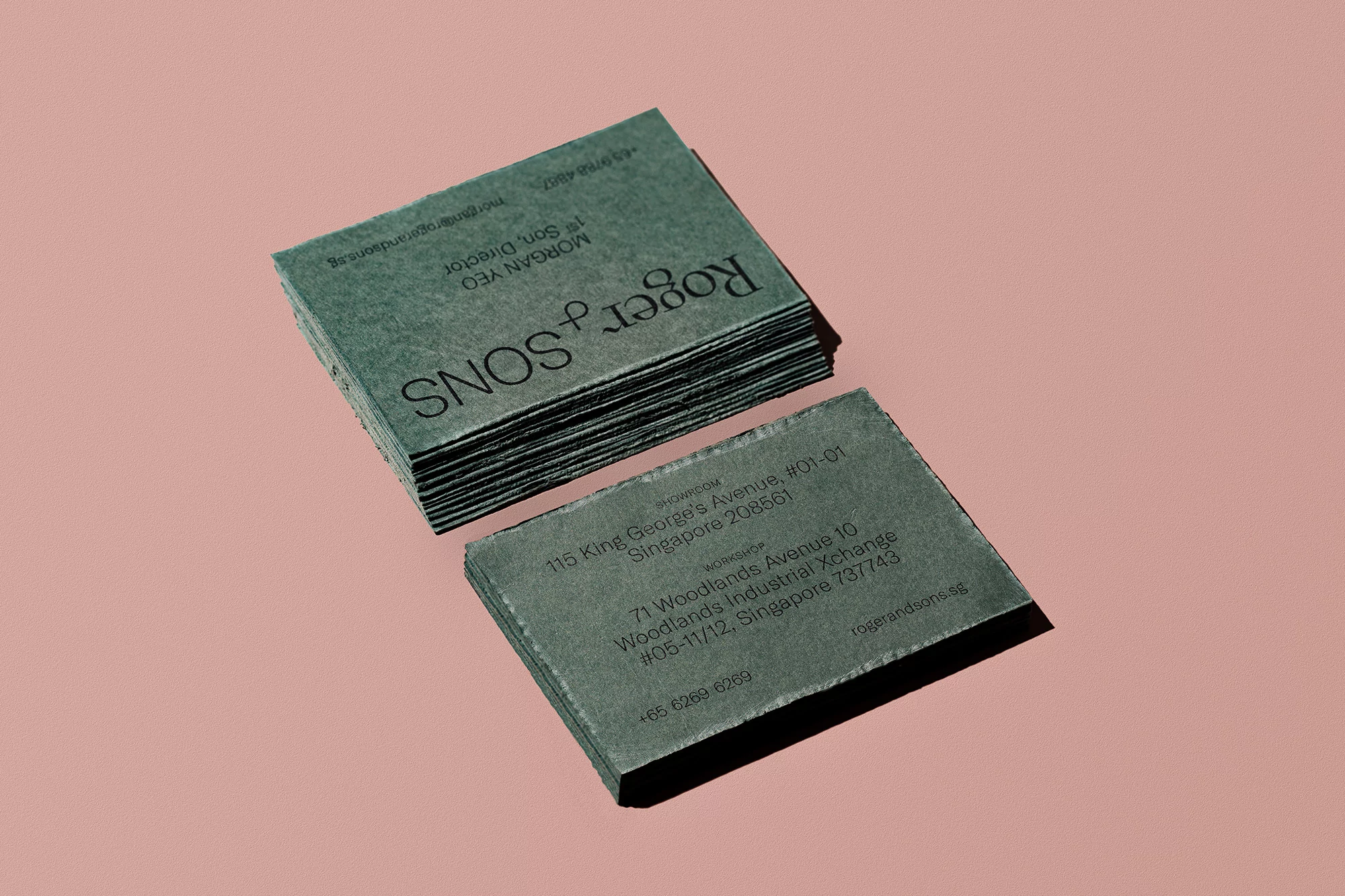 Stack of textured green business cards on a pink surface, featuring the company name Roger & Sons and contact information.