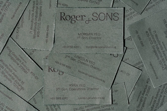 Close-up of textured business cards with the company name Roger & Sons and employee contact details in grey tones.