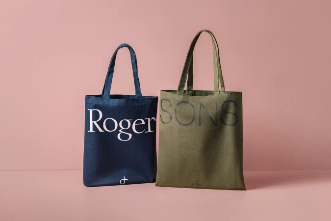 Two canvas tote bags with printed typography displayed against a solid pink studio background.