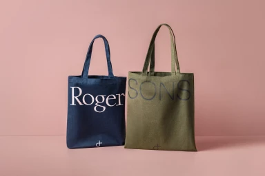 Two canvas tote bags with printed typography displayed against a solid pink studio background.