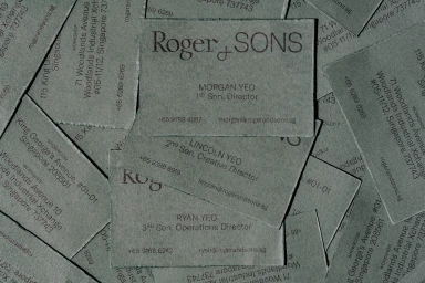 A flat lay arrangement of textured grey paper business cards for Roger and Sons featuring names and contact details.