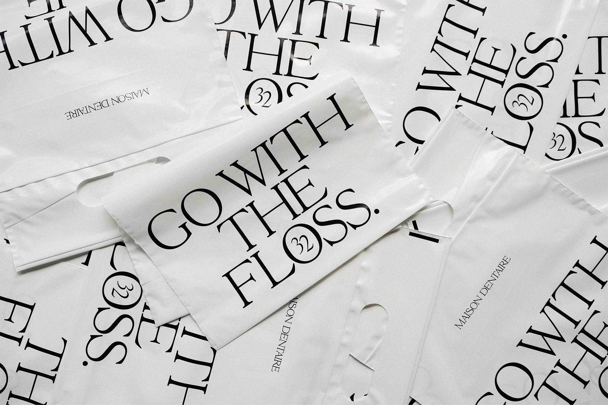 Multiple white plastic bags with black text that reads 'Go With The Floss' and 'Maison Dentaire' are arranged in a studio shot.