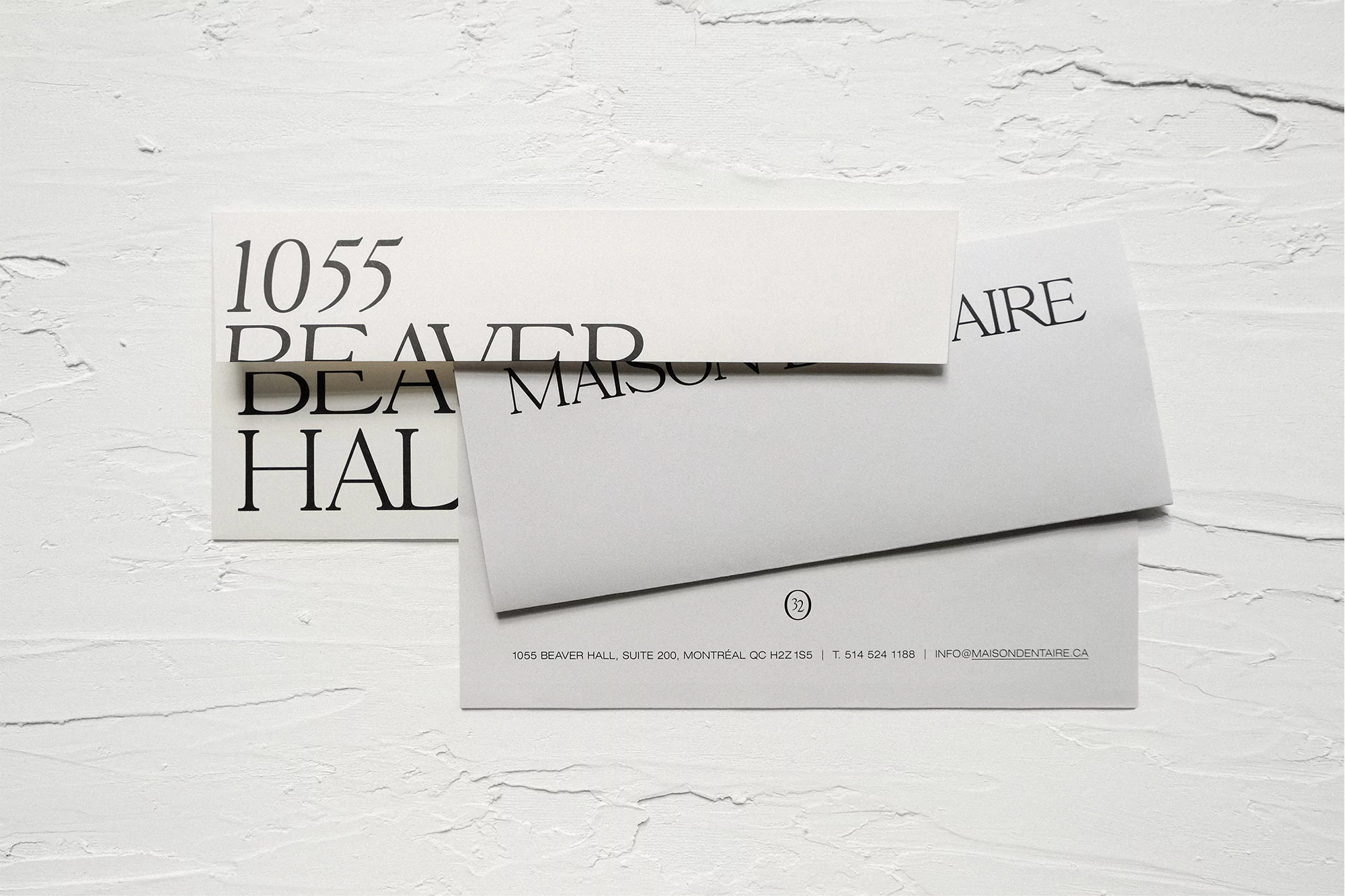 Promotional shot featuring a stack of minimalist white business cards and envelopes on a textured white surface with elegant typography.