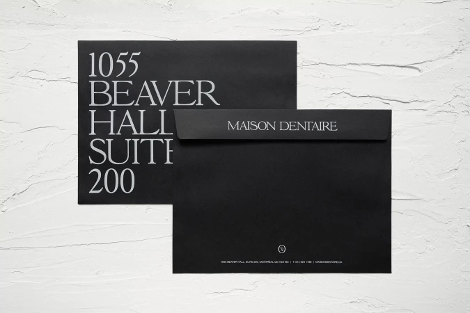 Close-up of two black envelopes, one with '1055 Beaver Hall Suite 200' in white text, the other with 'Maison Dentaire' text.