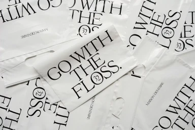 Stack of white plastic retail bags with black typography reading go with the floss and maison dentaire brand name.