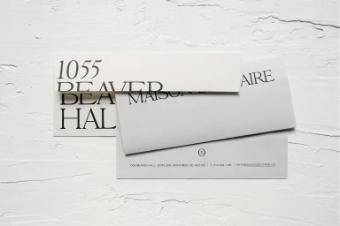 Branded stationery envelopes with serif typography resting on a textured white plaster surface.