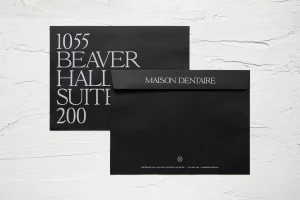 Two black envelopes with elegant serif typography resting on a textured white plaster surface.