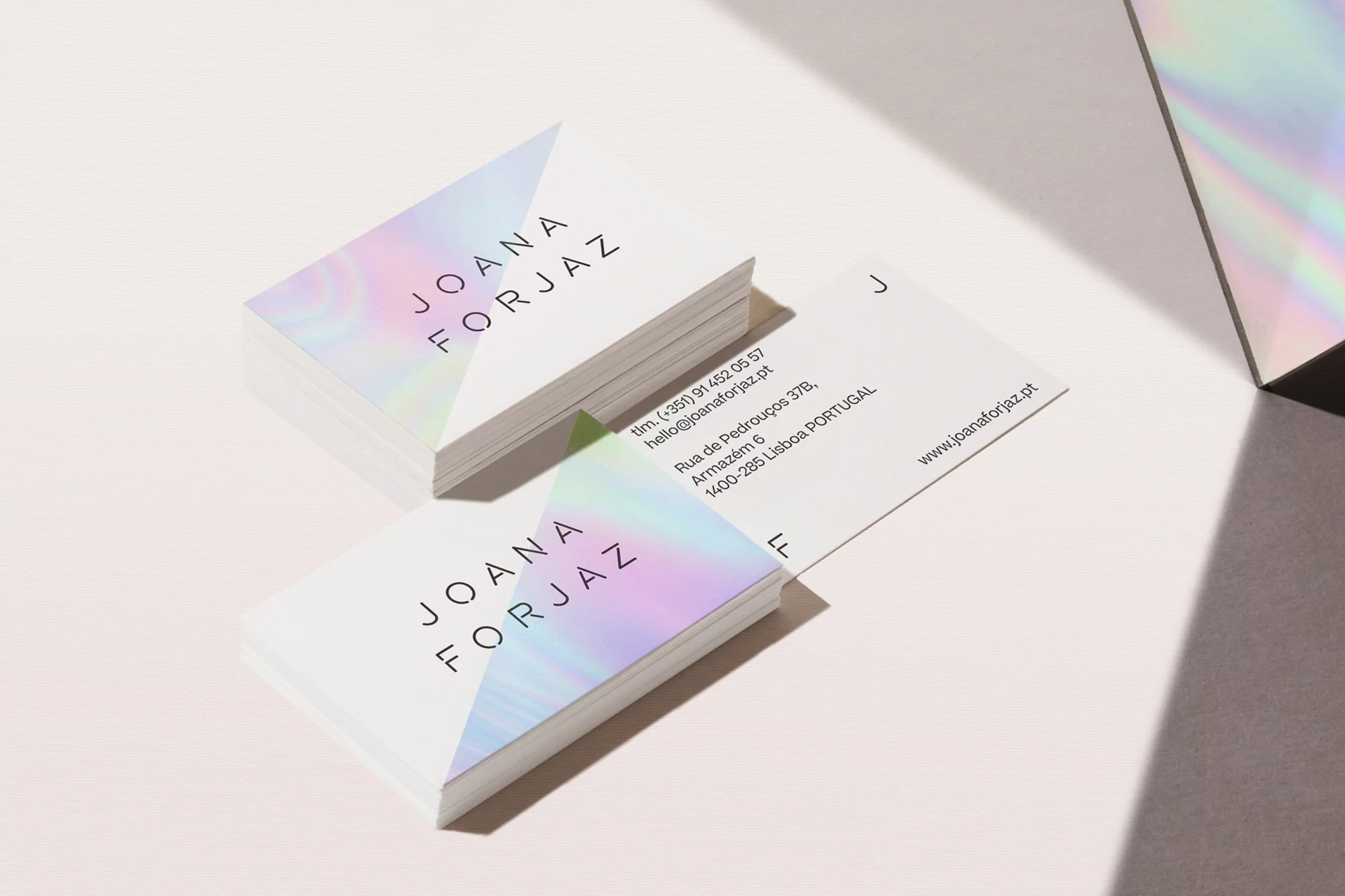Stack of business cards with a holographic geometric design, resting on a white surface with a soft shadow effect. Clean, modern design.