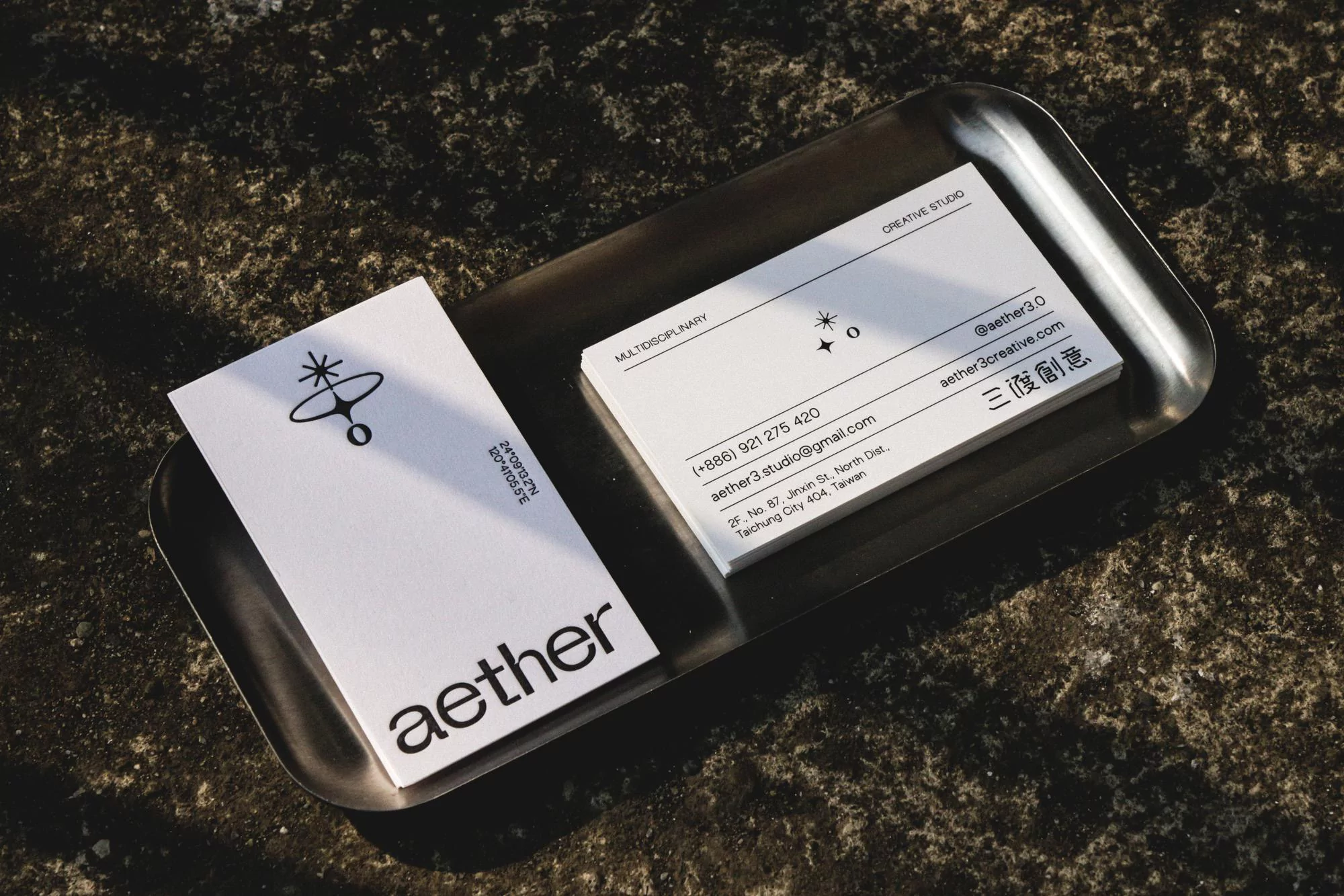 Elevated shot of business cards on a metal tray. Minimalist design with black text on white cards, under soft, natural light.