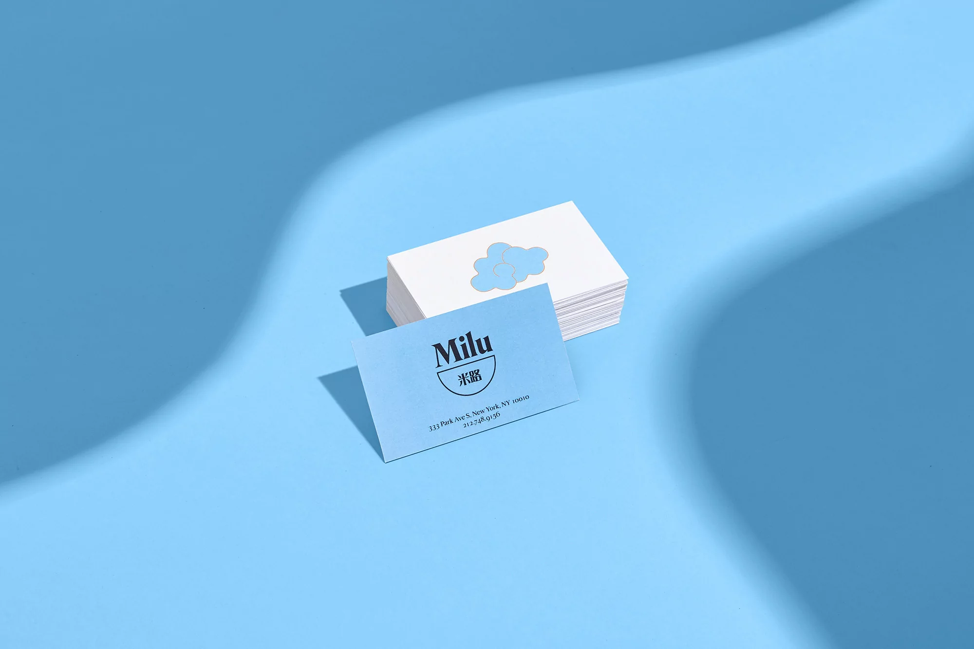 Stacked business cards with blue cloud logo and Milu brand typography resting on a blue surface under soft shadows