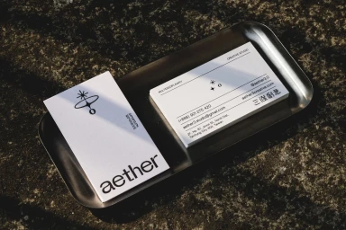 Minimalist white business cards featuring a celestial logo placed on a metallic tray over a textured stone surface.