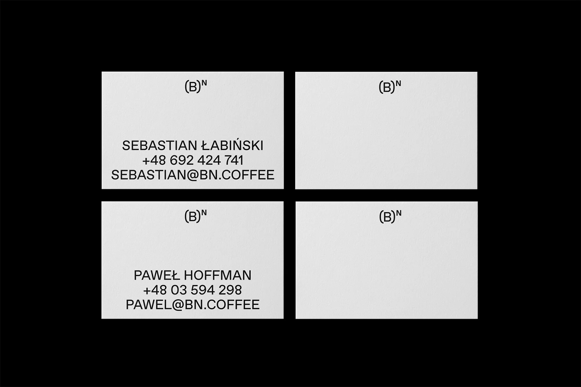 Close-up of four light gray business cards on a black surface. Each card features simple black text with names and contact information.