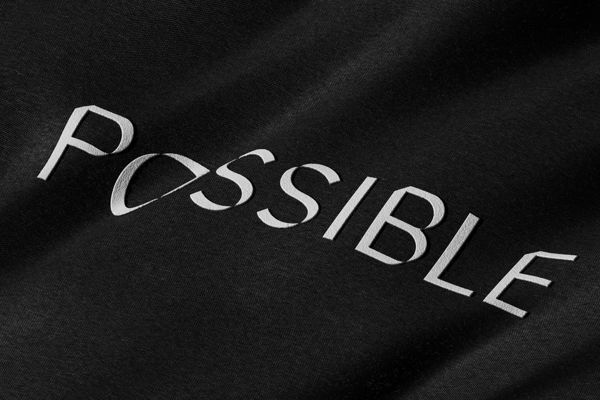 Embroidered "Possible" text on black fabric, simple studio shot, close-up.